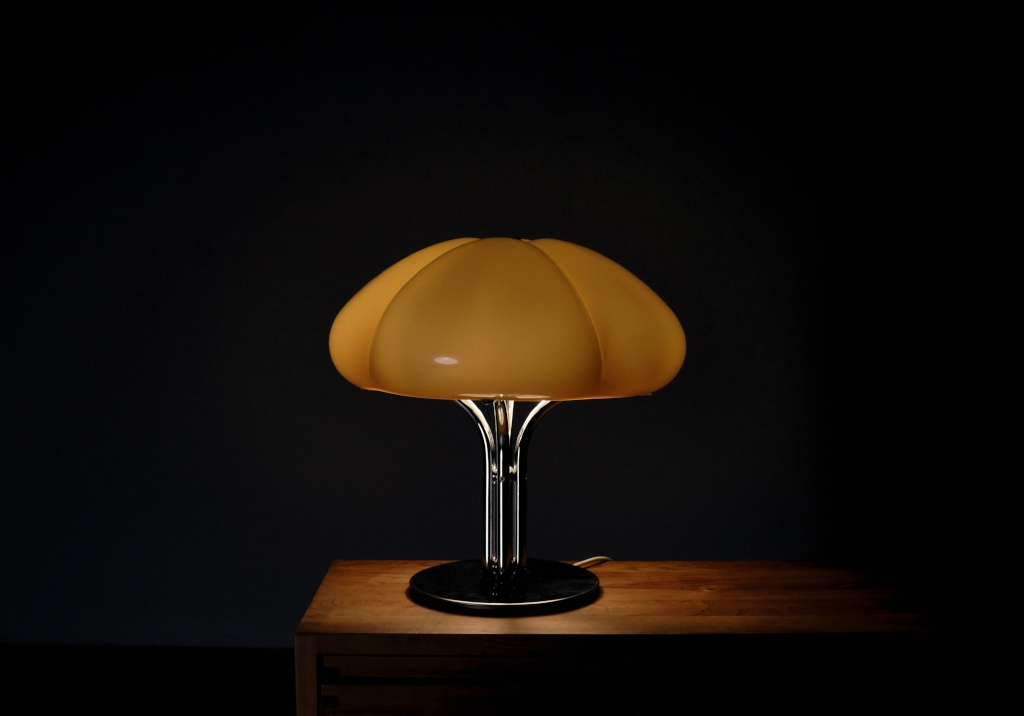 Quadrifoglio Lamp Edited by Guzzini: view of the lit lamp, the soft light falls delicately on a wooden surface